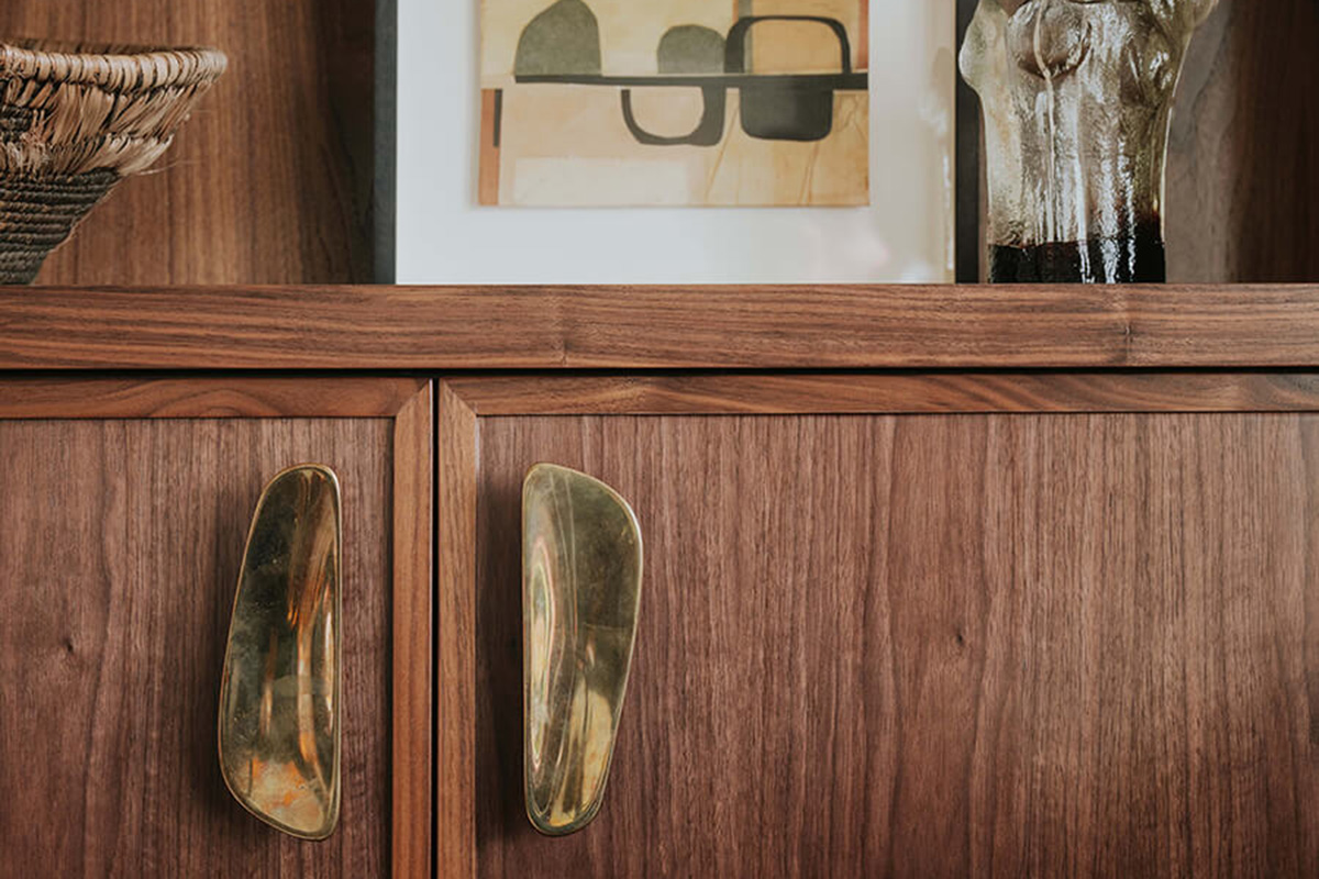 Brass cabinet handles layered against rich walnut timber joinery decorated with African-inspired décor and art.