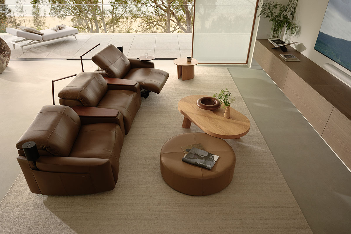A modular lounge recliner sofa in chocolate brown leather with timber shelves for remotes and magazines.