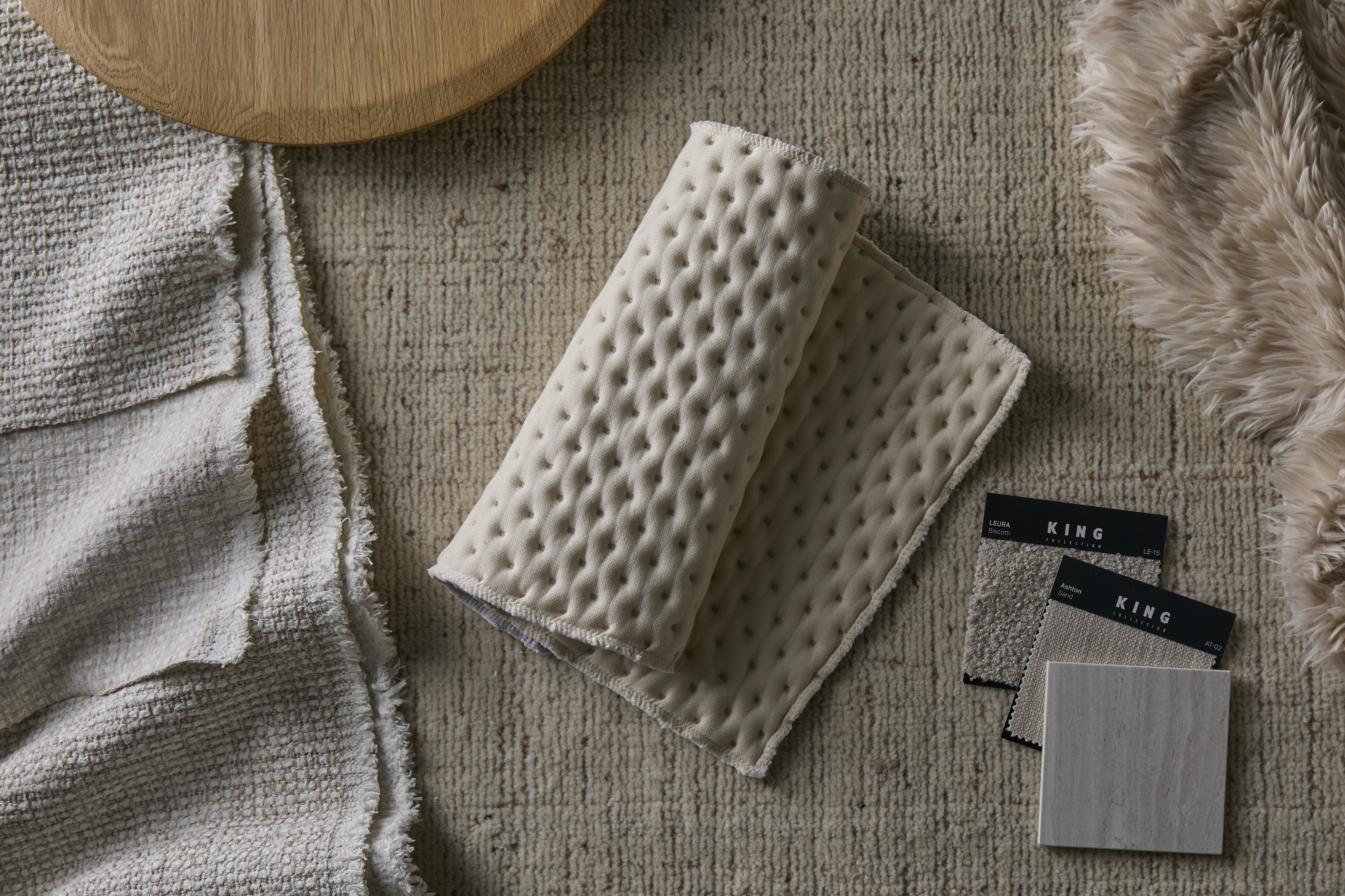A flat lay showcasing a curated arrangement of soft textiles including bouclé and faux fur, complemented by light stone finishes.